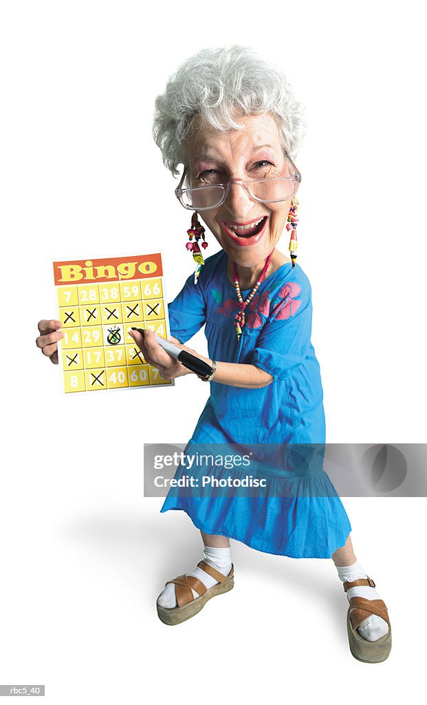 A caucasian grandma wearing glasses and a blue mu mu smiles while she holds up her bingo chart to show five x's in a row