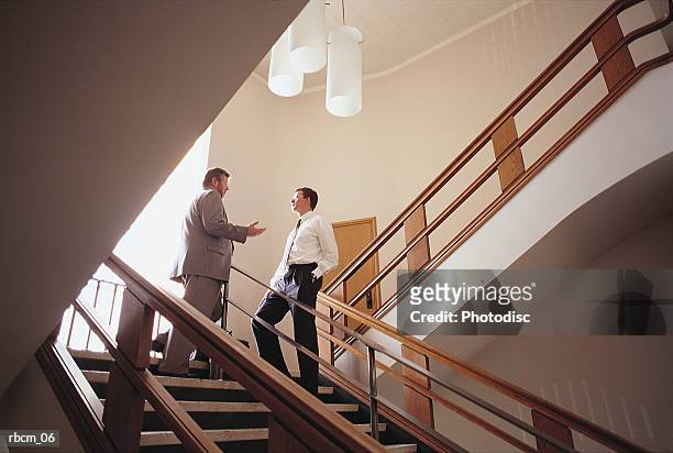 a businessman dressed in a suit stands atop a flight of stairs while talking to another man dressed in a white shirt - aother stock pictures, royalty-free photos & images