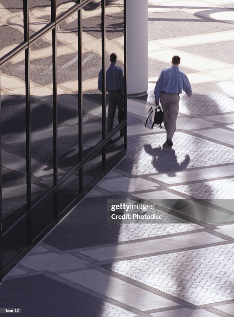 A BUSINESS MAN WALKS ALONG A GLASS BUILDING WHILE CARRYING A BRIEF CASE