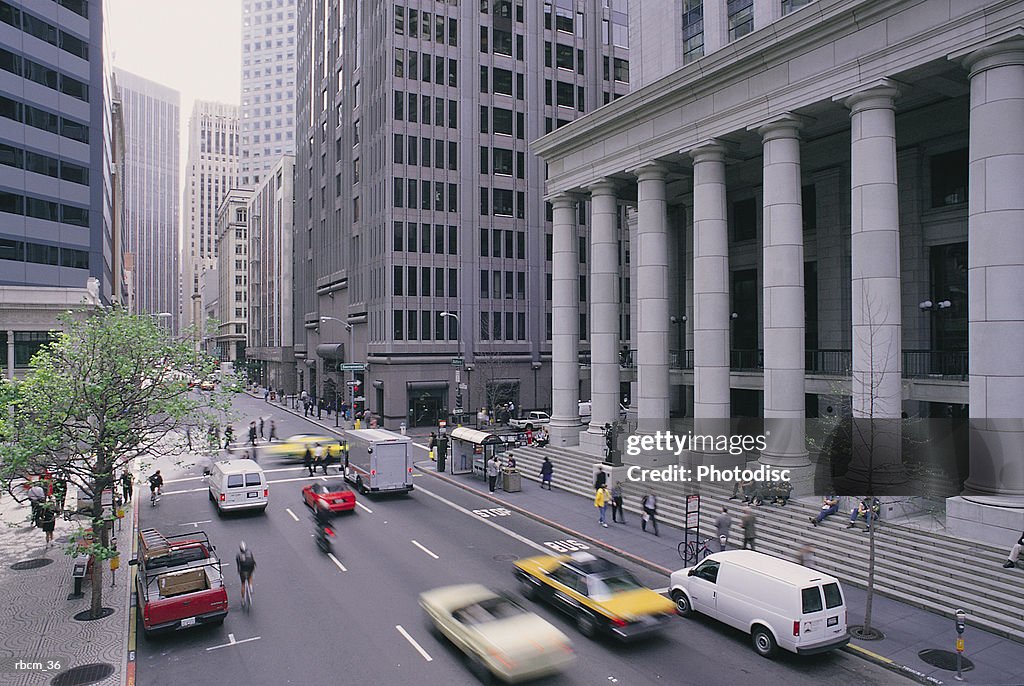 PEOPLE ON FOOT AND IN CARS TRAVEL ALONG ROADS SURROUNDED BY BUILDINGS AND TREES