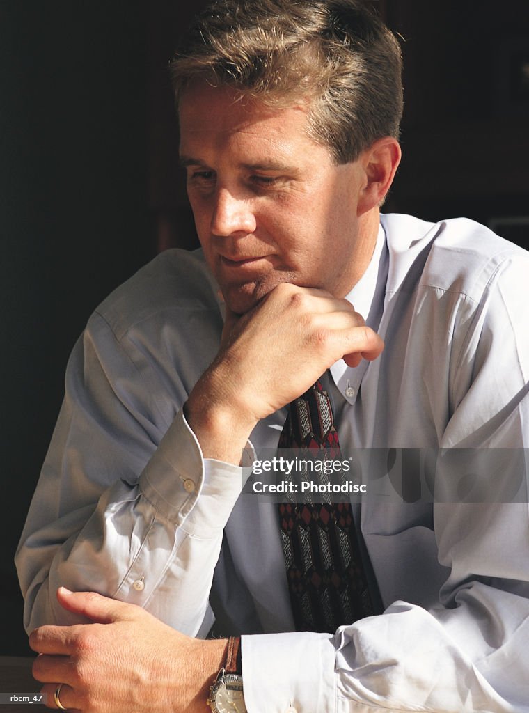 A BUSINESSMAN IN A BLUE SHIRT AND TIE SITS AS HE THINKS.