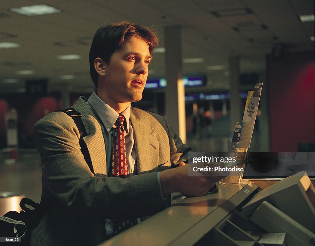 A BUSINESSMAN DRESSED IN A GRAY SUIT HANDS OVER HIS PLANE TICKET WHILE STANDING IN AN AIRPORT