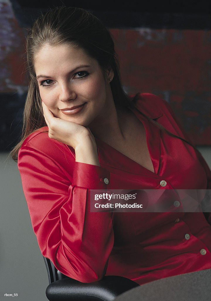 A BUSINESSWOMAN DRESSED IN A RED SHIRT SMILES AS SHE SITS IN A CHAIR