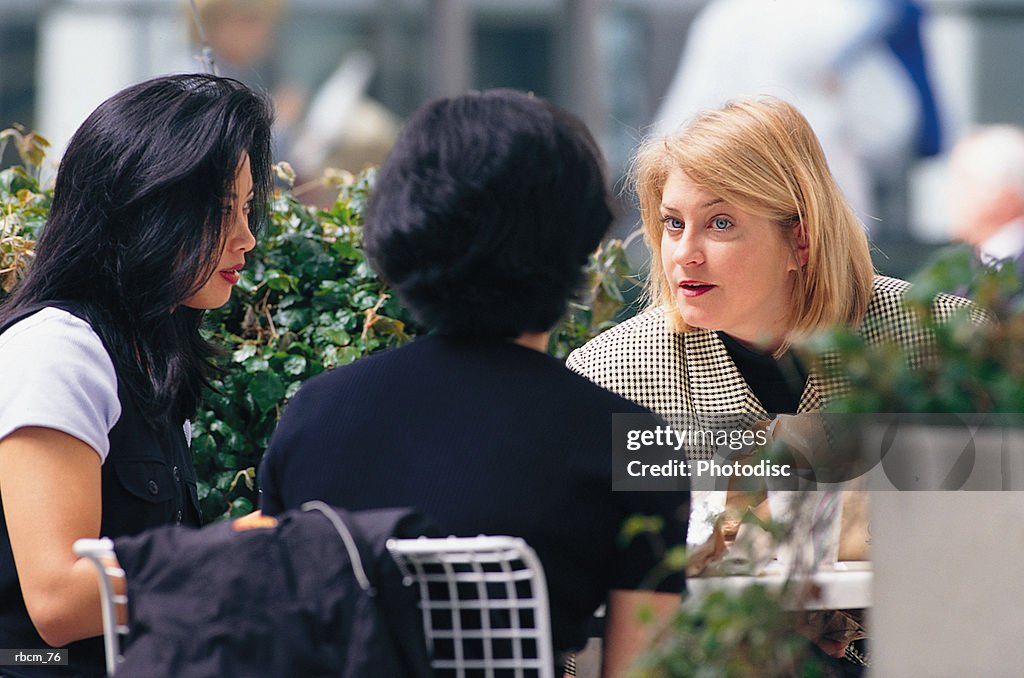 Three brunette businesswomen converse while sitting outside and eating lunch