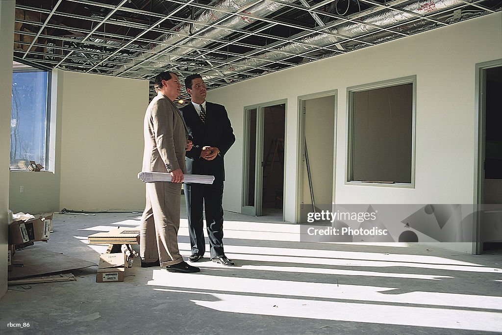 Two suited businessmen dressed in suits stand in an unfinished office talking