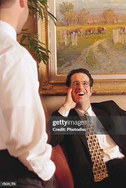 a man dressed in a black suit smiles while sitting as he listens to another dressed in a white shirt - aother stock pictures, royalty-free photos & images