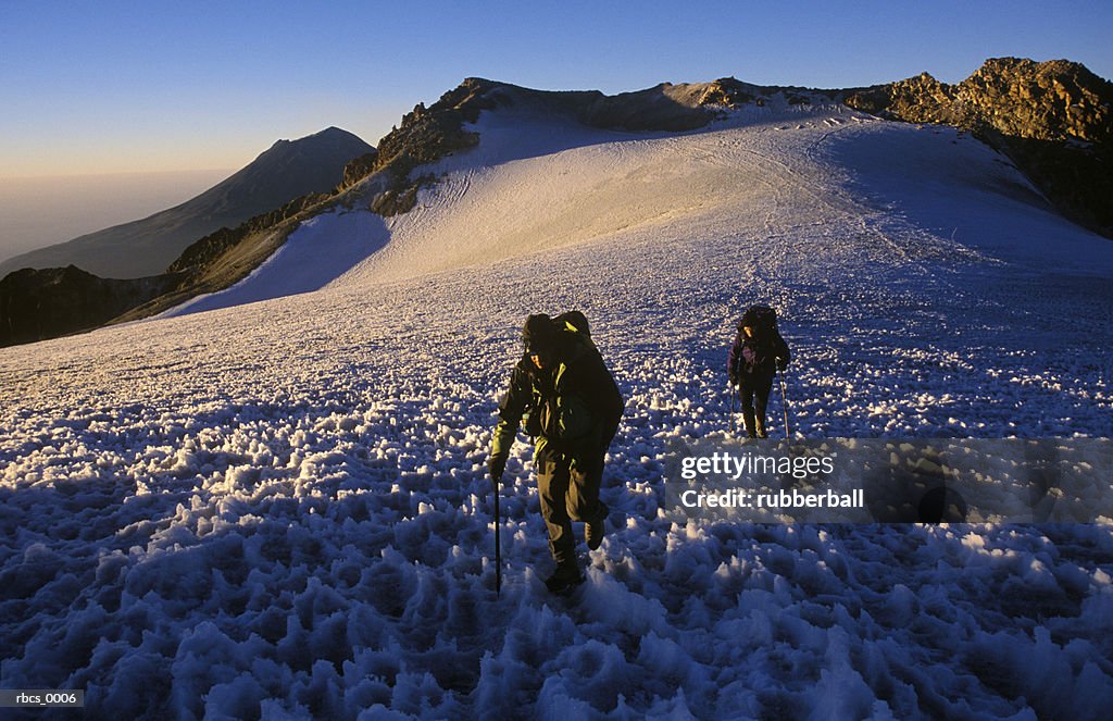 Lifestyle shot of a two adult males as they slowly climb up a snow covered mountain