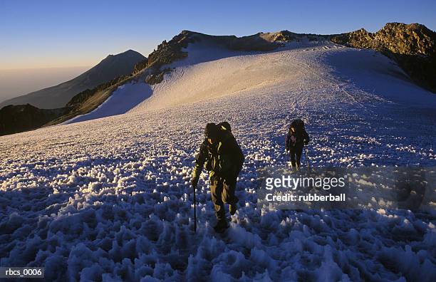lifestyle shot of a two adult males as they slowly climb up a snow covered mountain - gestalt stock-fotos und bilder