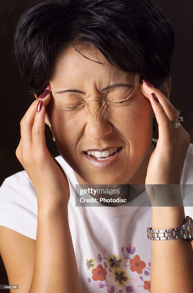 A young asian woman with short hair holds her fingers to her temples and squints her eyes shut as if in pain