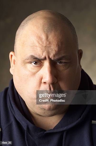 a large sized caucasian man wearing a blue sweatshirt has a shaved head and is scowling with pursed lips - shaved head ストックフォトと画像