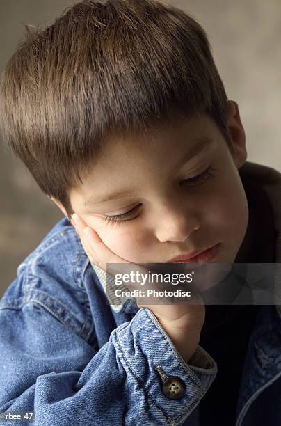 a young caucasian boy in a jean jacket is leaning his head on his hand as he closes his eyes - hand on head ストックフォトと画像