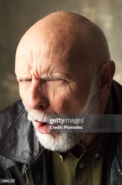 an elderly bald caucasian man with a white beard is wearing a leather jacket and scowling with eyes narrowed - angry bald screaming man ストックフォトと画像