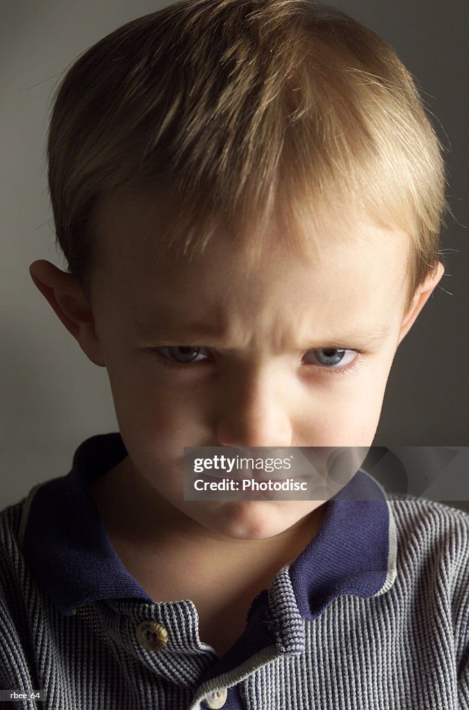 A cute little caucasian boy with light brown hair is wearing a stripped blue shirt and pouting