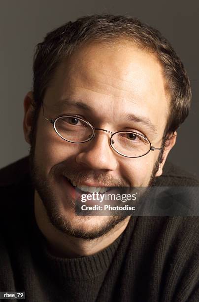 a middle age caucasian man with a happy smile has a short beard and is wearing glasses and a dark sweater - happy stockfoto's en -beelden