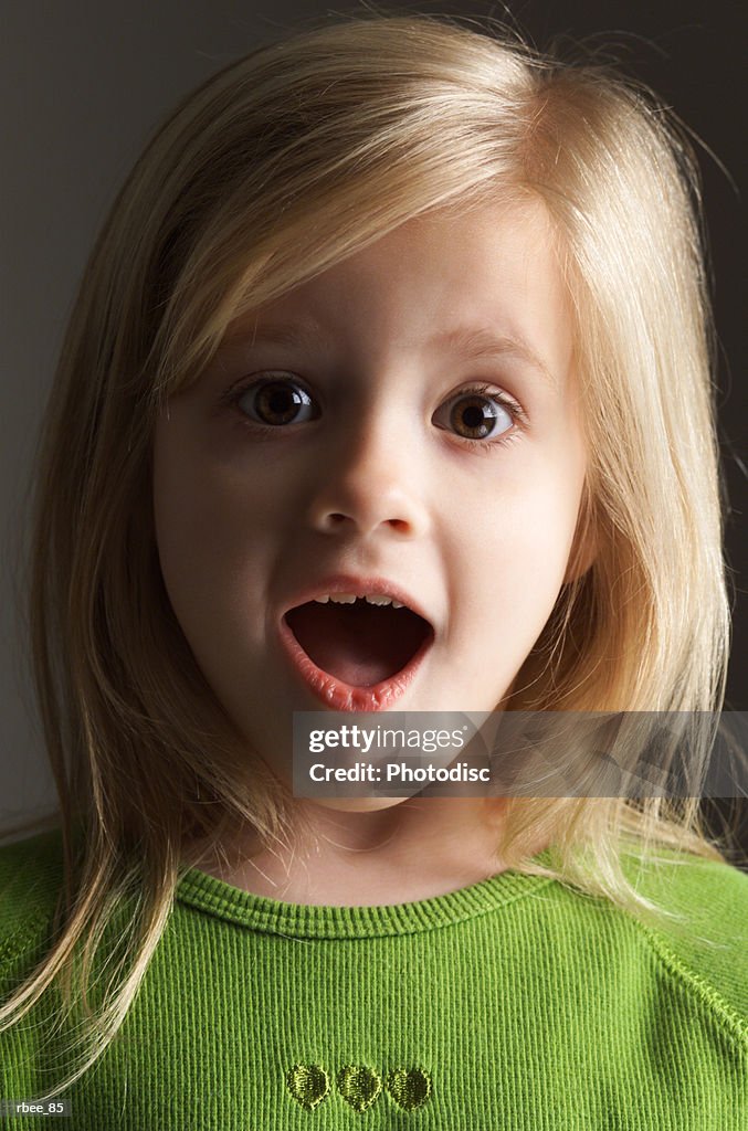 A little blond girl in a green shirt stares wide eyed and open mouthed with an expression of surprise
