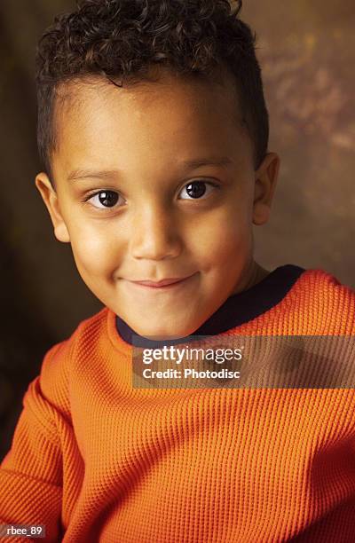 a cute little african american boy wearing bright orange is grinning mischevously with his mouth closed - mouth smirk stock pictures, royalty-free photos & images