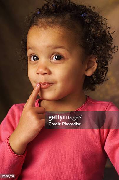 a pretty little african american girl wearing a pink shirt is looking up as she touches her finger to her lips - little finger stock pictures, royalty-free photos & images