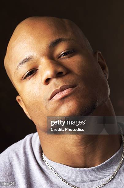 a young black man with a goatee in a gray t-shirt tilts his bald head back and looks steadily with an expression of defiance - bald stock-fotos und bilder