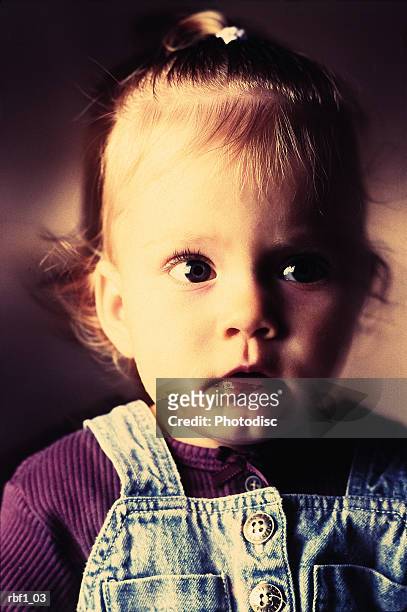 baby girl with thin slightly curly hair wearing light denim overalls and purple shirt looks to her left into the darkness with a curious scared questioning and confused look on her face - curly stock pictures, royalty-free photos & images