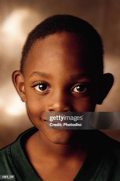 happy african-american boy with big brown eyes and very short black hair wearing a green shirt gives the camera a slight smile - happy stockfoto's en -beelden