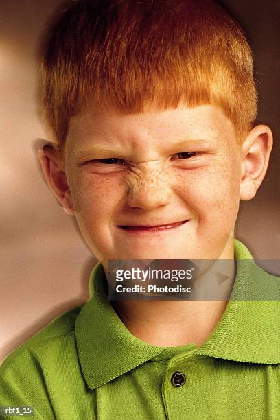 happy little young boy with red hair and freckles wearing a lime green golf shirt makes a funny face at the camera scrunching up his nose and squinting. - happy stockfoto's en -beelden