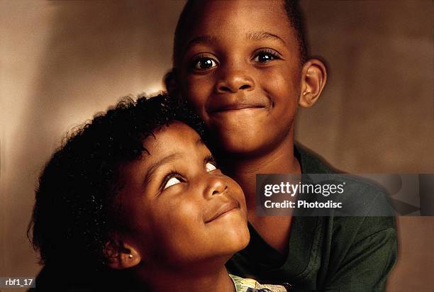two happy children an african-american boy who is wearing a green shirt and girl who appear to be brother and sister with black hair joyfully sit together as the boy smiles at the camera and the little girl looks up to the boy with affection - happy stockfoto's en -beelden