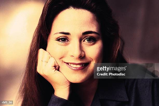 happy female woman with brunette hair wearing a dark shirt rests her chin on her hand while smiling - happy stockfoto's en -beelden