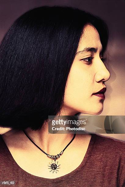 happy female woman with shorter straight dark hair and red lipstick wearing a maroon dress and necklace looks to her left revealing her stunning profile - maroon hair stock pictures, royalty-free photos & images