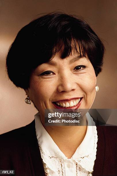 happy business-like asian woman with short black hair wearing a white shirt black jacket and earrings smiles pleasantly - happy stockfoto's en -beelden