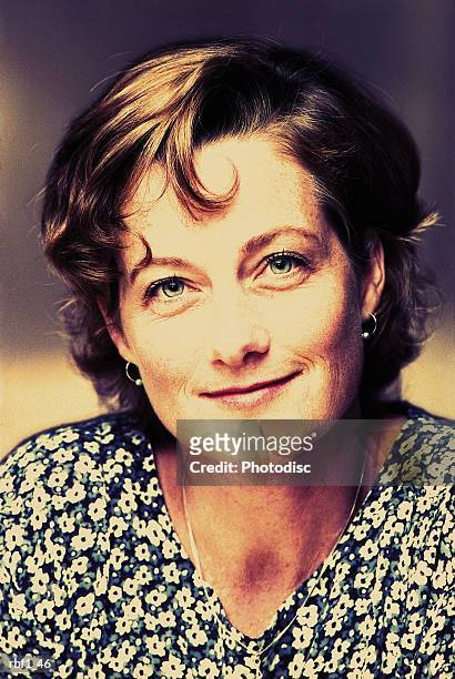 happy woman female with short curly brown hair and a very pretty face wearing a green and white floral shirt or dress smiles softly - happy stockfoto's en -beelden