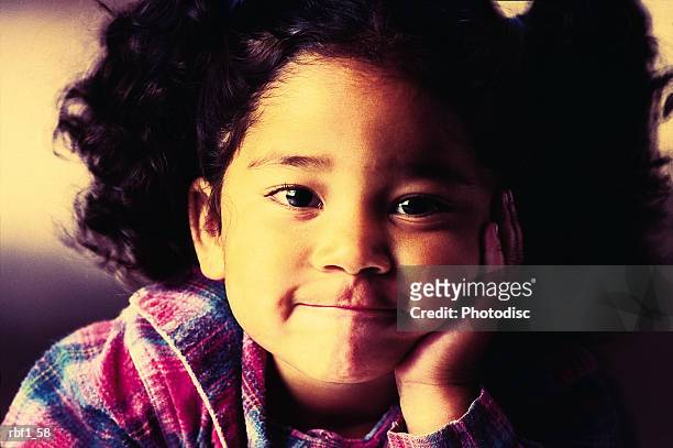 cute asian girl with her curly black hair pulled up in pigtails wearing a pink and blue plaid shirt grins with her mouth closed as she rests her cheek on her hand - curly stock pictures, royalty-free photos & images