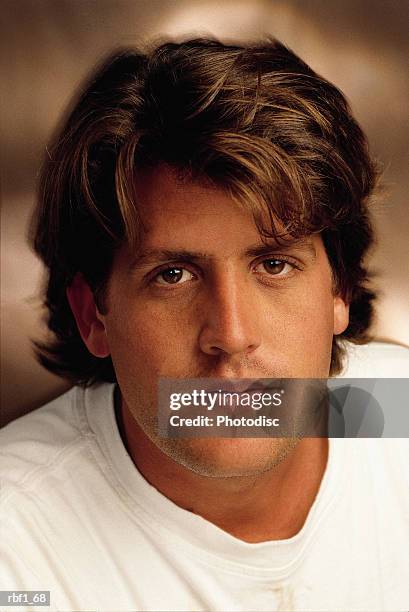 cool man male in 20_s with longer messy styled brown hair wearing a white tee shirt looks serious - tee shirt stockfoto's en -beelden