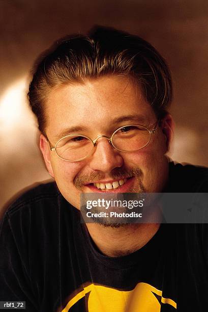 male man with dark blonde hair mustache and beard wearing a black tee shirt and glasses smiles - tee shirt stockfoto's en -beelden