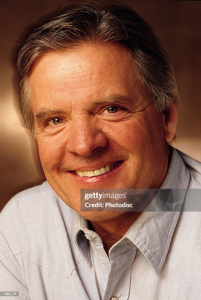 Happy middle aged man with graying hair wearing a light gray shirt smiles