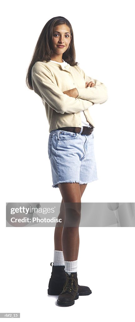 A young female teen in a tan sweater and shorts folds her arms and smiles