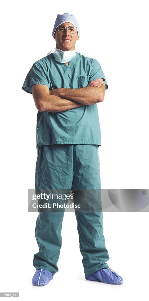 An adult male doctor in scrubs and a surgical mask folds his arms and smiles
