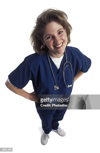 an adult female nurse in blue scrubs puts her hands on her hips and smiles up at the camera - arms akimbo ストックフォトと画像