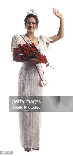 a young adult female beauty pageant contestant with flowers and a tiara waves at the camera - fusciacca foto e immagini stock