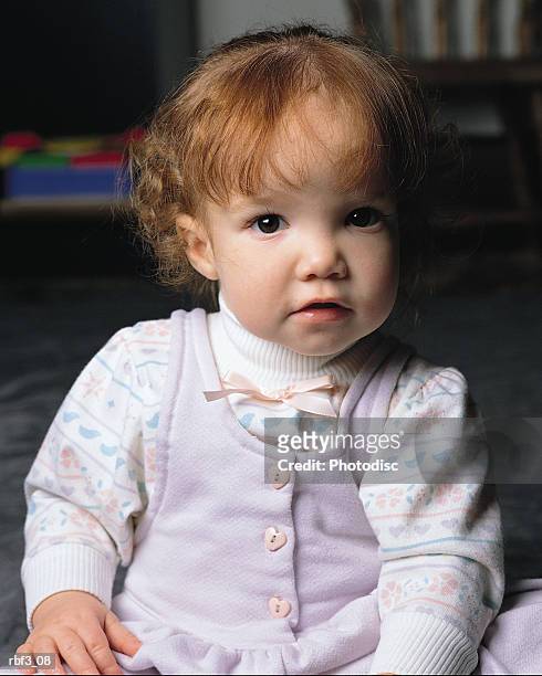 a brunette baby with curly hair and wearing a pink cotton jumper sits as she looks at the camera - curly stock pictures, royalty-free photos & images