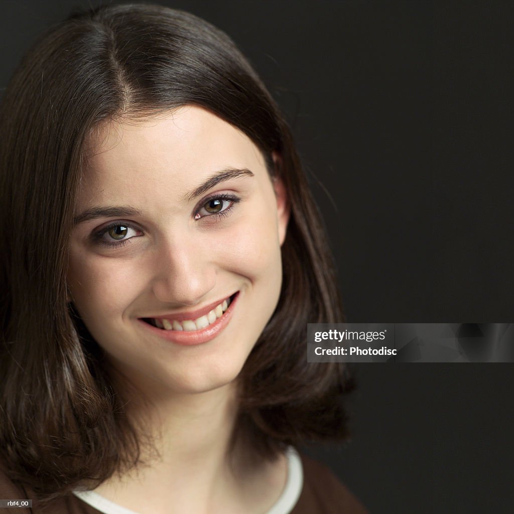 Portrait of a young caucasian girl in a brown shirt looks at the camera and smiles pleasantly