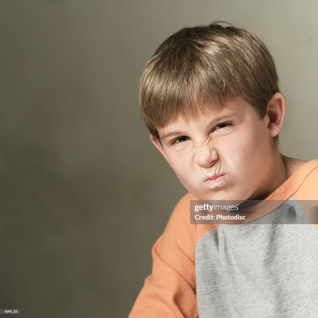 Portrait of a caucasian boy in a grey and orange shirt grimaces and frowns into the camera