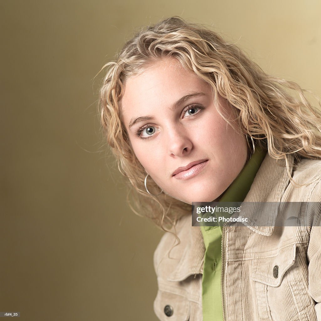 Portrait of a blonde caucasian teenage girl in a green shirt and tan jacket as she smiles slightly