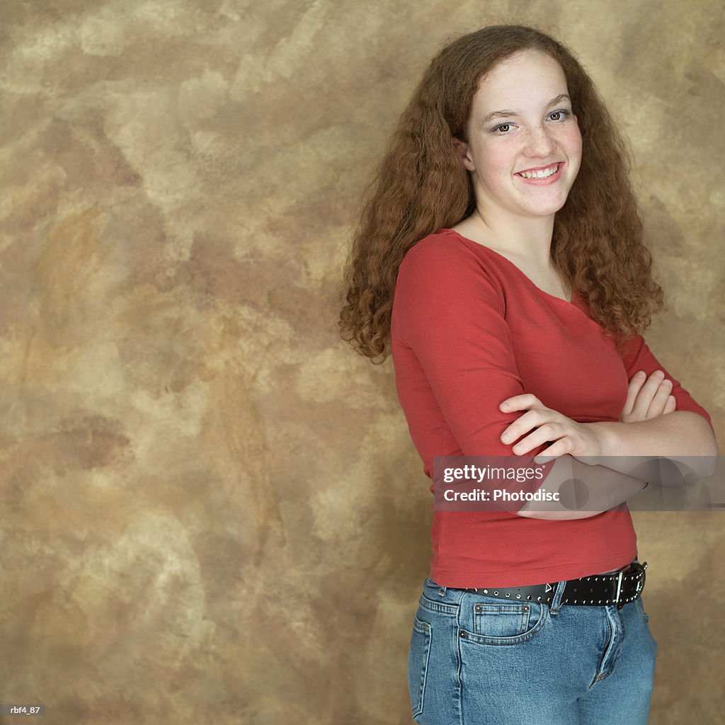 Portrait of a teenage caucasian redheaded girl in a red shirt as she folds her arms and smiles