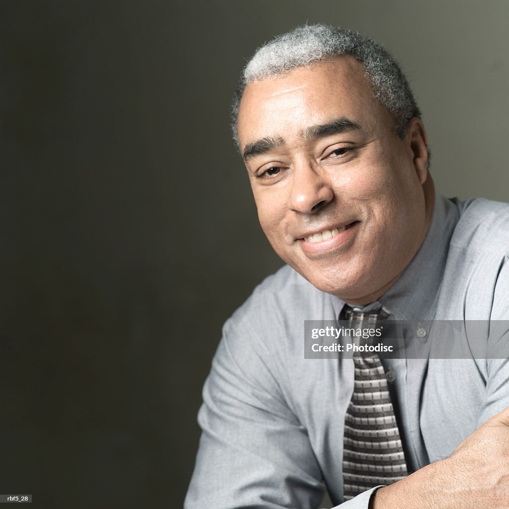 Portrait of an older african american man in a grey shirt and tie as he folds his arms and smiles