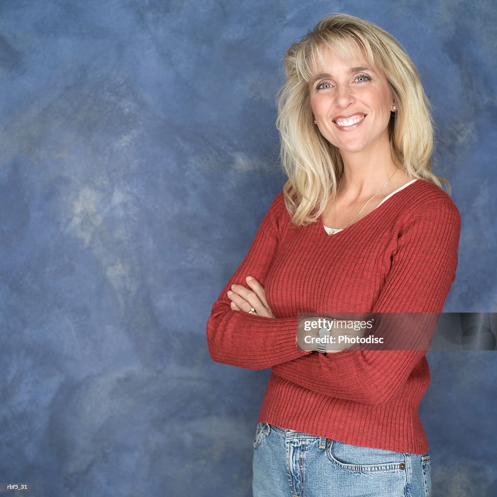 Portrait of a blonde caucasian woman in a red sweater and jeans as she folds her arms and smiles