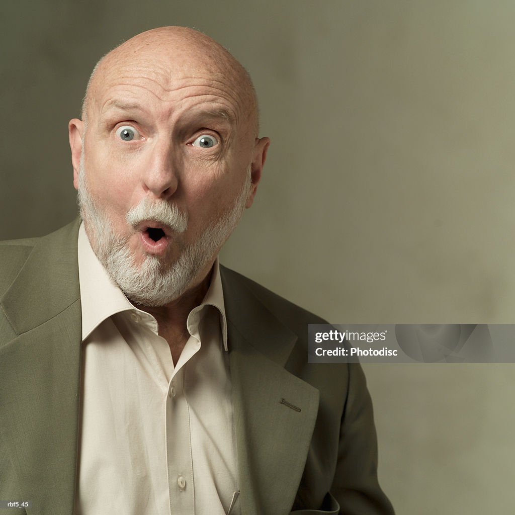 Portrait of an elderly bearded caucasian man in a olive green suit as he looks shocked and surprised