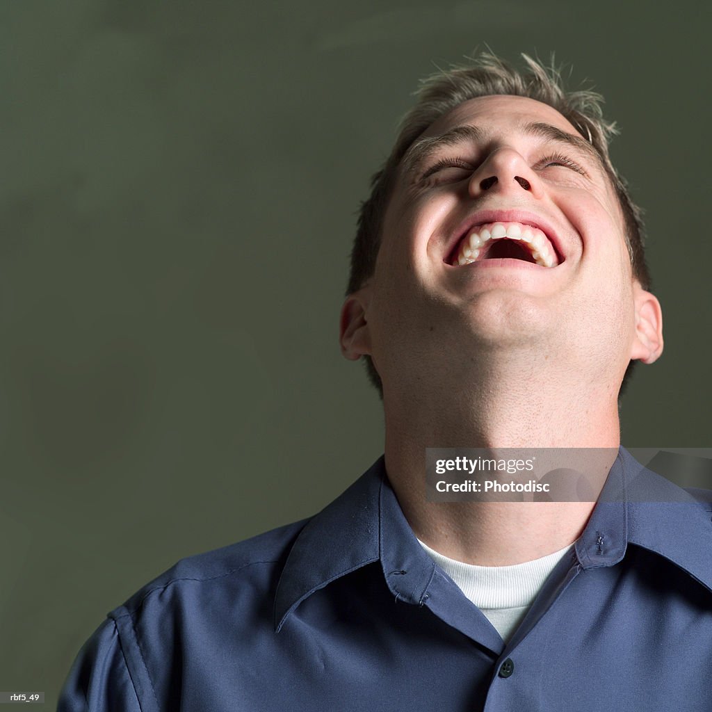 Portrait of a young caucasian man in a blue shirt as he throws his head back and laughs