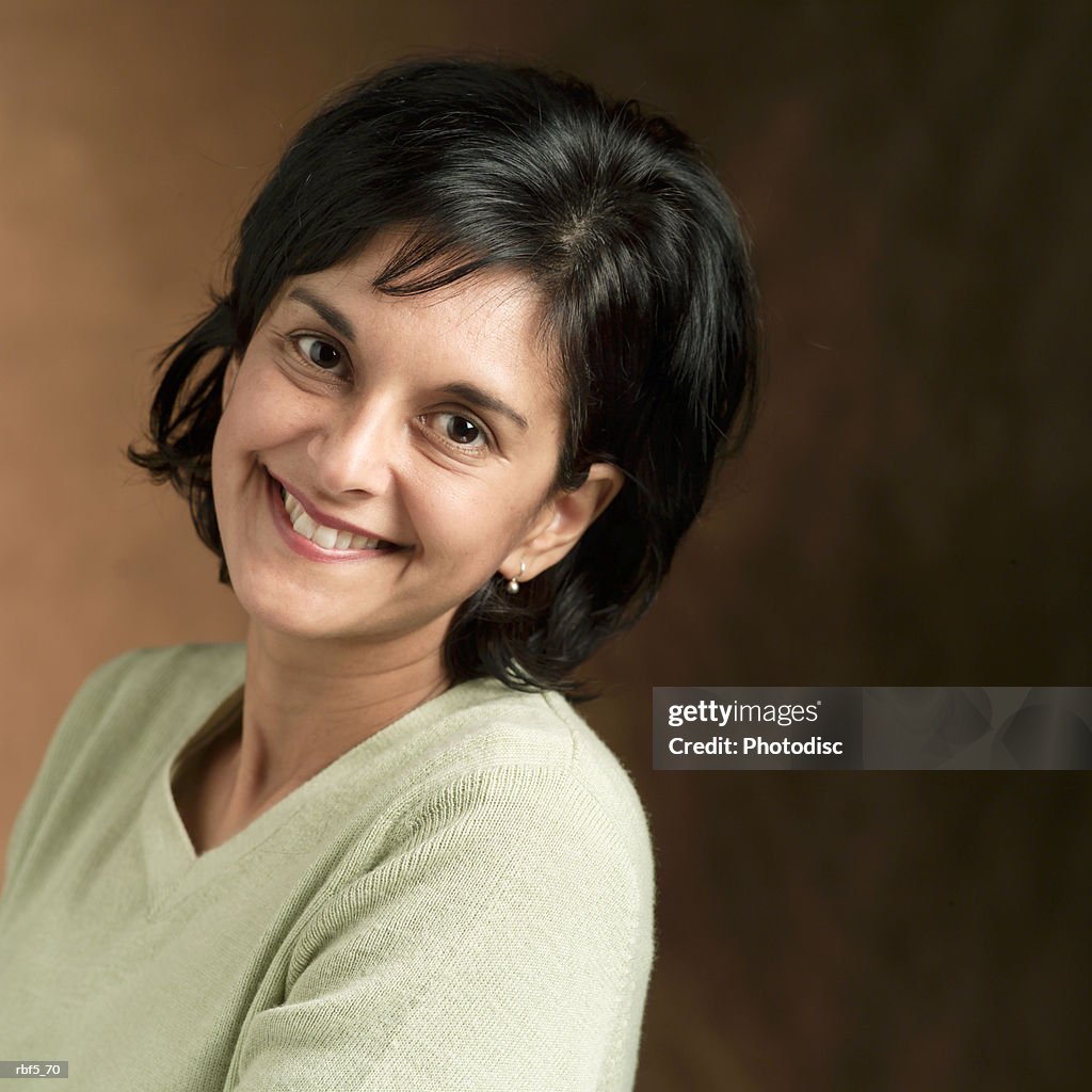 Portrait of an ethnic looking woman in a tan sweater leans back and smiles into the camera