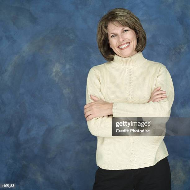 a portrait of a caucasian woman wearing a yellow turtleneck stands with arms folded as smiles - turtleneck stock pictures, royalty-free photos & images