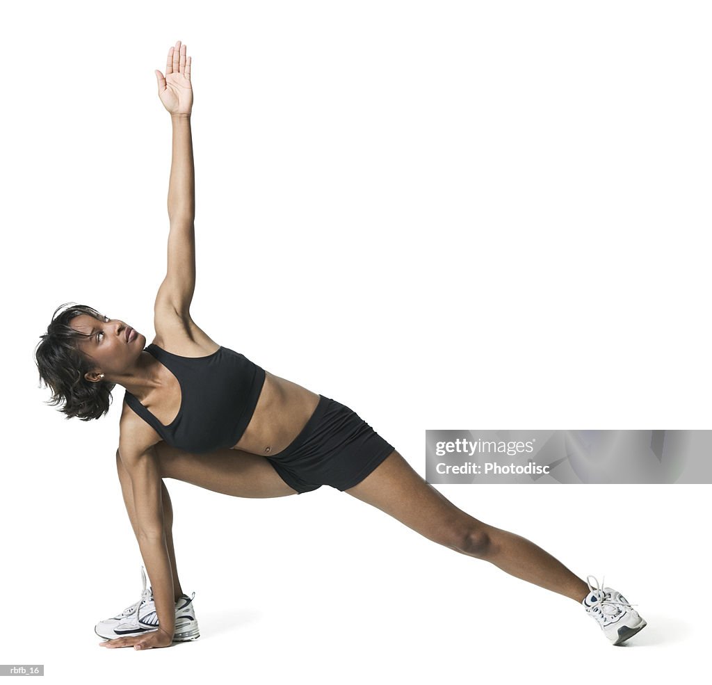 Full body shot of a young adult woman in a black workout outfit as she stretches out in a yoga pose